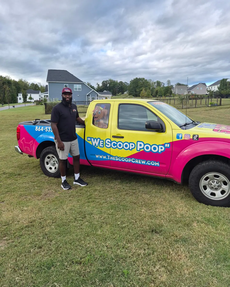 A Scoop Crew team member in a cap standing beside the pink and yellow branded truck